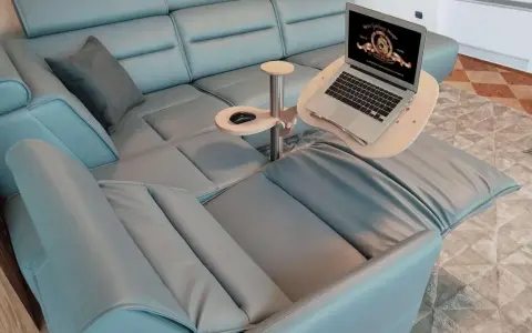 Comodo tavolino porta pc in legno e metallo, agganciato a un divano in pelle azzurra, con laptop aperto e mouse.