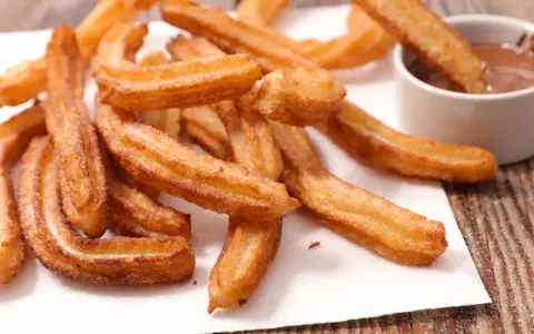 Goldbraune Churros, frisch frittiert, mit Zucker bestreut. Ein Churro wird in eine Schüssel mit Schokoladensauce getunkt. Ein echtes Churros Rezept Original.