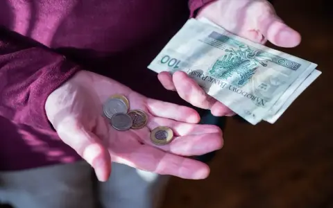 Dłonie trzymające polskie banknoty i monety. Zastanawiasz się, ile wynosi dodatek do emerytury za warunki szkodliwe?