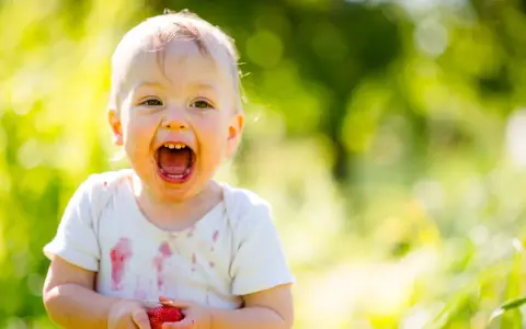 Uśmiechnięte 1.5 roczne dziecko nie mówi mama, ale z radością trzyma truskawkę.