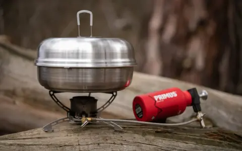En primus kaffepanna på en campingkök med en röd gasbehållare. Perfekt för fika i naturen.