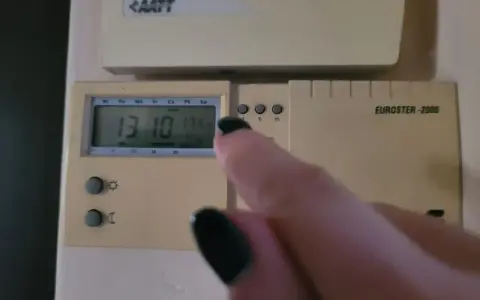 Dłoń z czarnym lakierem na paznokciach dotyka termostatu, sterowanie piecem gazowym. Na wyświetlaczu 13:10 i 17.5°C.
