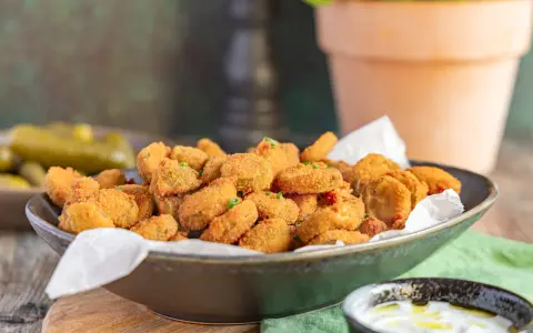 Knusprig frittierte Gurkenscheiben, **fried pickles**, in einer Schale, daneben ein Dip und ganze Gewürzgurken.