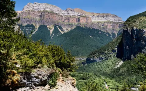 Paisaje de Ordesa y Monte Perdido con niños explorando senderos entre bosques frondosos y imponentes montañas.