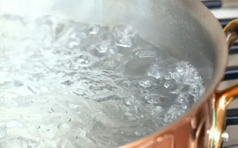 Woda wrze w miedzianym garnku, tworząc bąbelki. Czas gotowania zależy od tego, ile się gotuje woda.