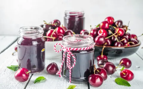 Słoiki z dżemem wiśniowym i świeże wiśnie na drewnianym stole. Idealne, by pokazać, co zrobić z wiśni.