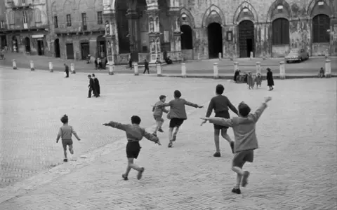 Bambini corrono in una piazza storica, un'immagine piena di movimento e gioia, perfetta come idee per foto.