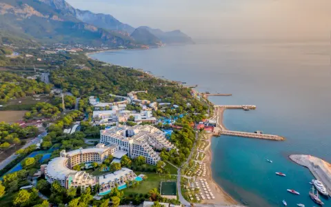 Widok z lotu ptaka na Rixos Sungate, luksusowy kurort nad turkusowym morzem, otoczony zielenią i górami.