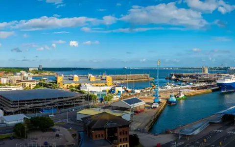 Vista panoramica del **southampton porto** con navi, gru e edifici moderni sotto un cielo azzurro con nuvole bianche.
