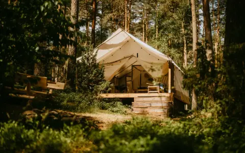 Namiot na Mazurach, otoczony lasem. Drewniana ławka i taras zapraszają do odpoczynku. Idealne miejsce na mazury pod namiot.