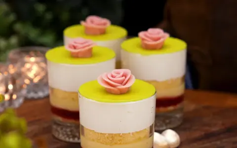 Fyra små prinsesstårta i glas, dekorerade med rosa marsipanrosor och gul marsipanlock. Vackert uppdukat med ljus i bakgrunden.