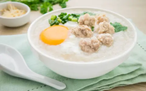Miseczka pysznego congee z mięsnymi klopsikami, jajkiem i szczypiorkiem. Idealne na rozgrzewający posiłek.