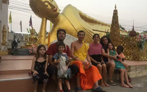 Familia disfrutando de un viaje a Asia con niños, sentados frente a una estatua dorada de Buda reclinado.