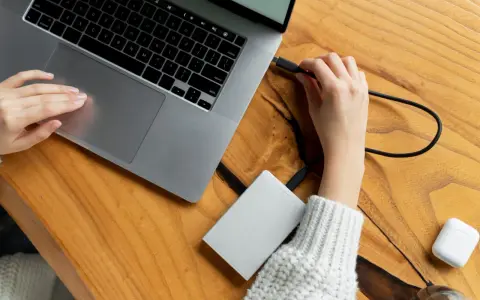 Podłączanie drugiego dysku SSD do komputera jest proste. Na zdjęciu widać, jak ręka podłącza kabel do laptopa, przygotowując się do rozszerzenia pamięci.