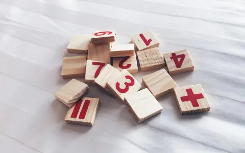 Drewniane klocki z cyframi i symbolami, jakby ktoś układał zadanie na **2 rok numerologiczny**.