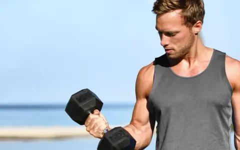 Mężczyzna ćwiczy biceps na plaży, zastanawiając się, ile serii na biceps w tygodniu da najlepsze efekty.