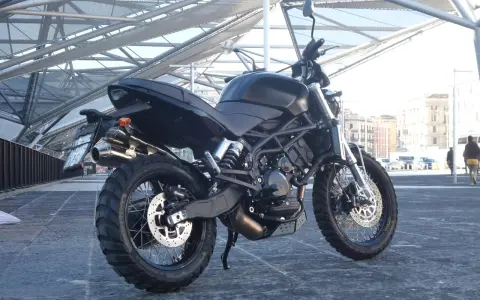 La Moto Morini Scrambler 1200, nera e imponente, si staglia sotto una struttura metallica moderna.