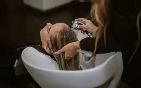 Una parrucchiera sciacqua i capelli di una cliente in un lavatesta, mostrando come lavare i capelli senza shampoo.