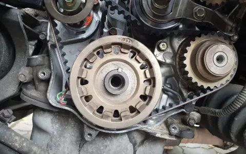 Zbliżenie na mechanizm silnika, widoczne koła zębate i pasek. Przygotowanie do wymiany rozrządu.
