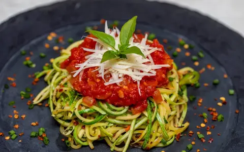 Deliciosa pasta con verduras, hecha de calabacín en espiral, cubierta con salsa de tomate y queso rallado.