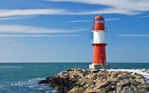 Roter Leuchtturm auf felsiger Mole am barth strand. Blaues Meer und Himmel mit Wolken.