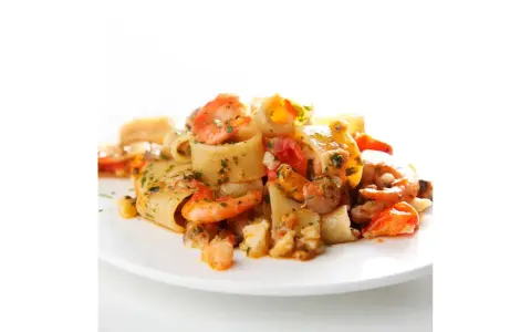 Piatto di calamarata allo scoglio con gamberi, cozze e pomodorini, condita con prezzemolo fresco.