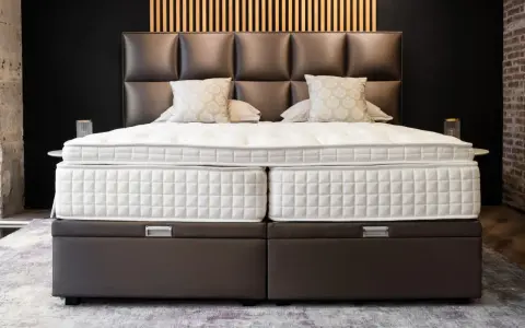 Lit, deux matelas blancs sur des sommiers marron. Le matelas trop grand pour sommier crée un léger débord.