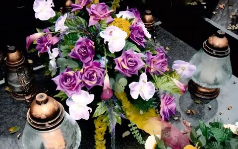 Piękne, fioletowe kwiaty przy urnie, ozdobione świecami, tworzą wzruszającą kompozycję.