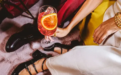 Elegancka kobieta z drinkiem, zastanawia się: martini co to? Złota biżuteria i czarne buty dodają szyku.