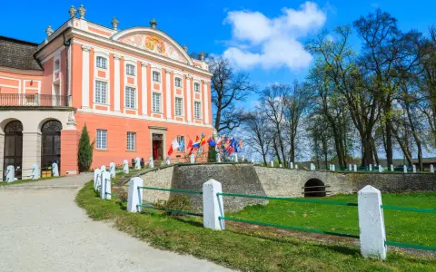 Pałac w Kurozwękach, z flagami narodowymi przed wejściem, zaprasza do odkrywania jego atrakcji.