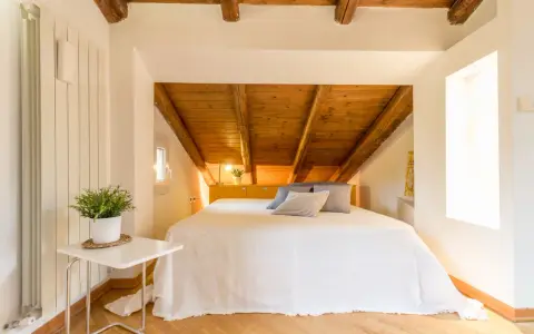 Accogliente camera da letto in mansarda con travi a vista in legno. Idee per un nido romantico e funzionale.