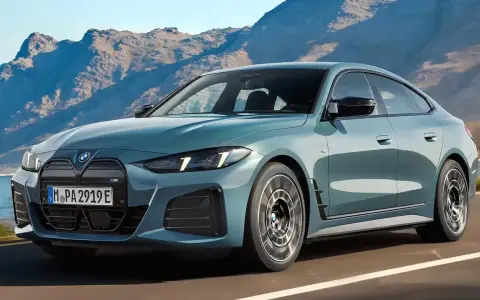 Der neue BMW i4 Facelift in einem eleganten Blau fährt auf einer Küstenstraße vor einer Bergkulisse.