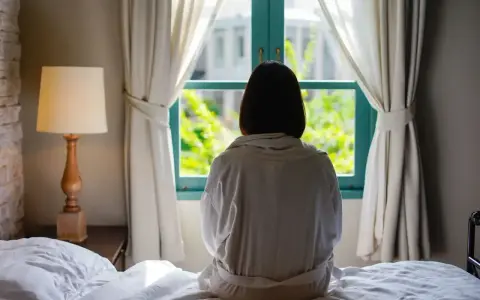 Osoba w szlafroku siedzi na łóżku, patrząc przez okno. Czy to objaw katatonii?