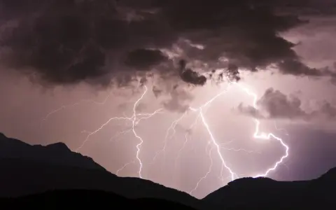 Gewitter in den Bergen: Blitze zucken durch dunkle Wolken über silhouettierten Gipfeln. Ein dramatisches Naturschauspiel.