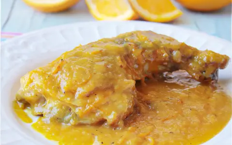 Delicioso pollo a la naranja, bañado en una salsa dorada y jugosa, con gajos de naranja frescos al fondo.