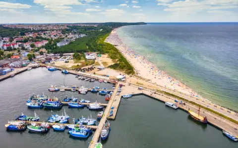 Port rybacki we Władysławowie, województwo pomorskie, tętni życiem. W tle rozciąga się plaża pełna turystów i morze.