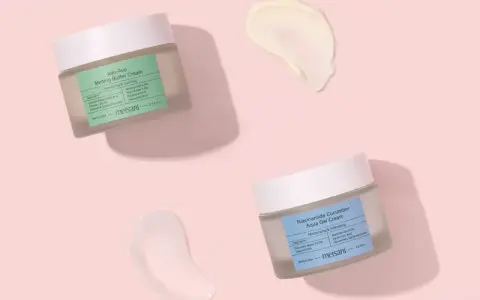 Due barattoli di crema viso Meisani, uno con niacinamide e burro, l'altro con niacinamide e cetriolo, su sfondo rosa. Perfetti per proteggere la pelle dal sole.