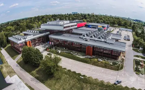 Nowoczesne budynki uczelni w Łodzi, otoczone zielenią, z widokiem na miasto.