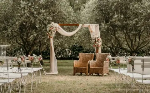 Un décor champêtre pour une célébration laïque : chaises blanches, arche fleurie, fauteuils en rotin sous les oliviers.