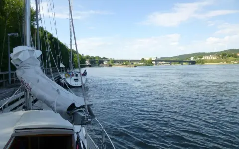 Segelbåtar vid kaj i Lilla Edet, en bro syns i bakgrunden över en bred flod.