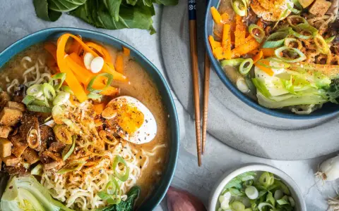Zwei Schüsseln dampfendes Miso Ramen mit Nudeln, Ei, Karotten, Pak Choi und Frühlingszwiebeln.