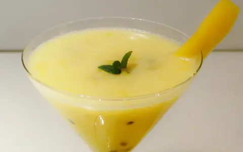 Orzeźwiający drink z marakują, ozdobiony listkiem mięty i kawałkiem mango.