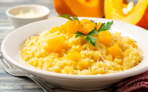 Un cremoso risotto de calabaza, adornado con trozos de calabaza y perejil fresco, espolvoreado con queso rallado.
