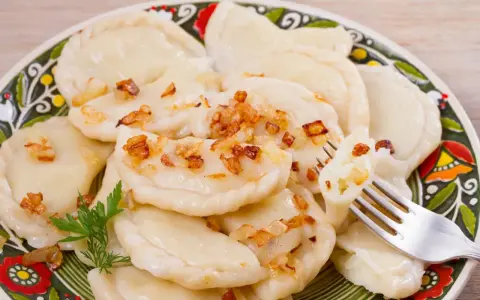 Pyszne pierogi ruskie z farszem Magdy Gessler, posypane skwarkami. Na talerzu z tradycyjnym wzorem.