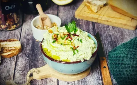 Cremiger Zucchini-Dip mit Pinienkernen und Kräutern, serviert mit geröstetem Brot.