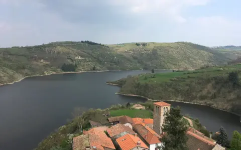 Villaggio pittoresco con tetti rossi e campanile affacciato su un lago serpeggiante, incastonato tra colline verdi vicino a Roanne, Francia.