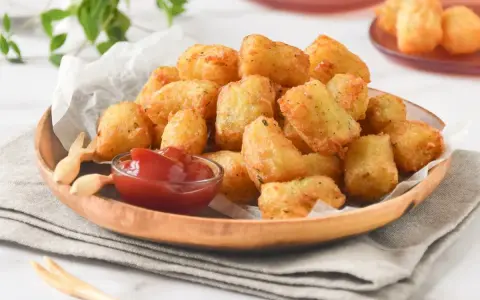 Tater tots dorados y crujientes servidos en un plato de madera con ketchup.