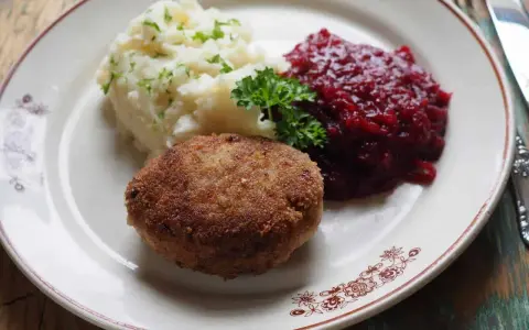 Kotlet mielony z ziemniakami i żurawiną, udekorowany natką pietruszki.