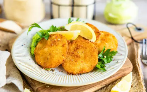 Knusprige Kohlrabi-Schnitzel auf einem Teller mit Erbsenpüree, Zitrone und Petersilie. Ein köstliches vegetarisches Gericht.