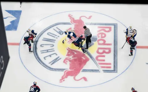 Hokeiści walczą o krążek na lodowisku z logo Red Bull. W hokeju są trzy tercje, a zawodnicy szykują się do kolejnej.